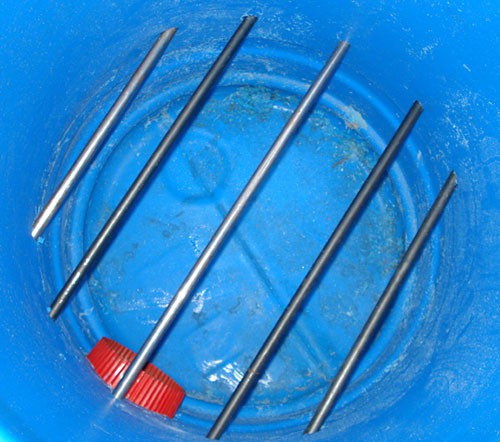 Five metal rods are inserted in parallel through the bottom half of a plastic barrel