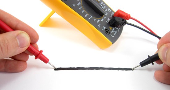 Probes of a multimeter touch opposite ends of a black line painted on a piece of paper