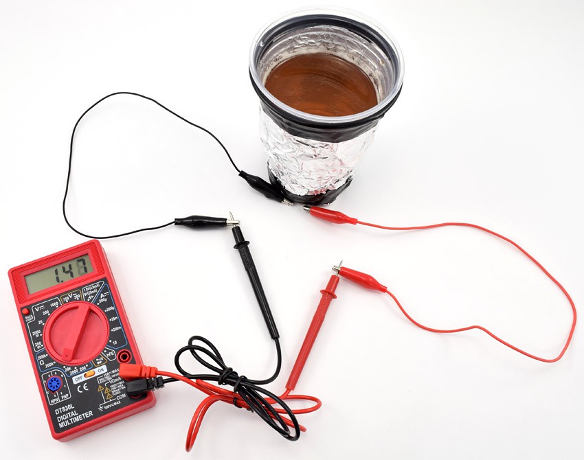 Multimeter probes connect to two leads of a photoresistor that is embedded in the bottom of a cup wrapped in foil