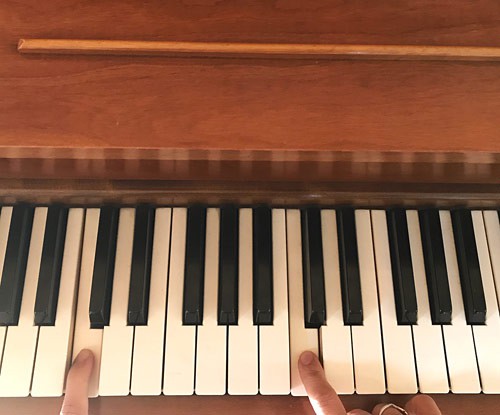 Two fingers press down on the C2 and C3 keys on a piano