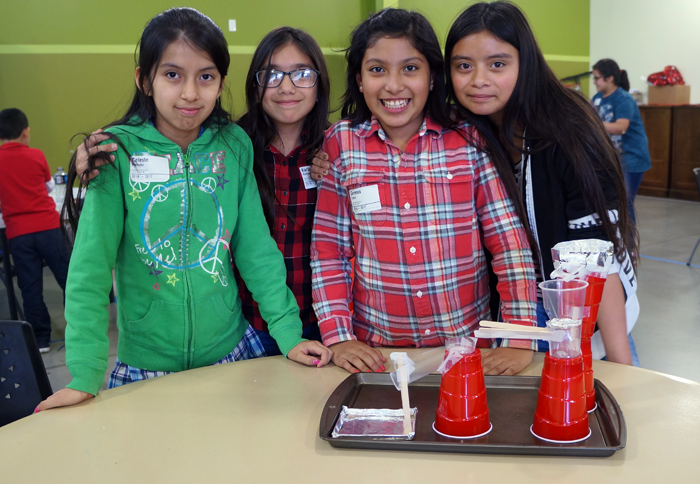 Four students next to two towers made from plastic cups, tape and aluminum foil