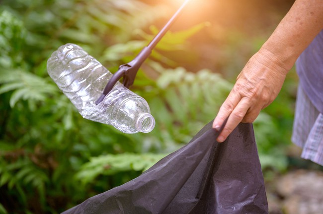 A person picking up a plastic bottle with a trash grabber