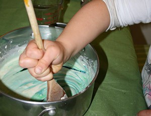 A wooden spoon is used to stir a green mixture in a pot