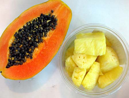 Half a papaya next to a bowl of pineapple chunks