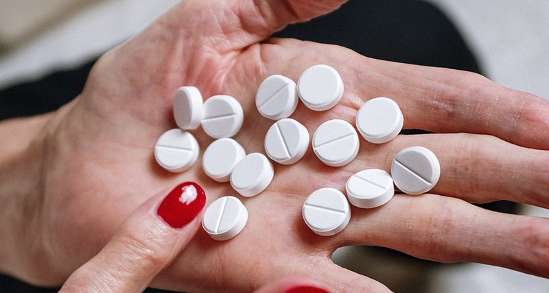 Hands of an elderly woman with many white pills across her palm. 