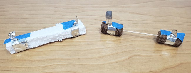Two options for building the conductivity sensor. One is a long rectangular piece of foam with two strips of aluminum foil wrapped around its ends, secured with tape. The other is two corks separated by a toothpick, with a strip of aluminum foil wrapped around each cork, secured by tape.  