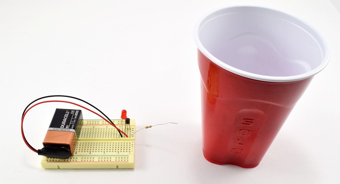 An electric field detector circuit on a breadboard next to a plastic cup