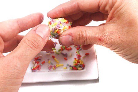 Hands holding a buttered aluminum ball and rolling it in sprinkles.