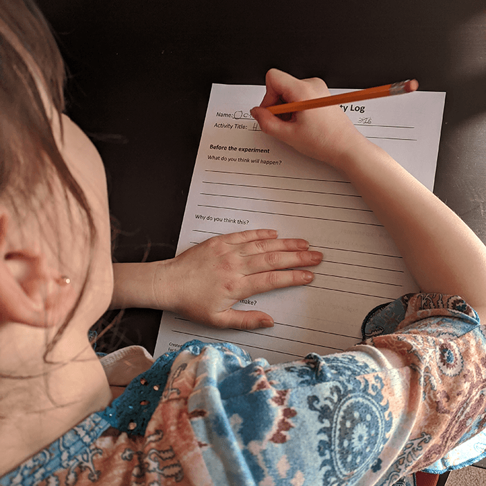 Girl writing science experiment observations on a worksheet