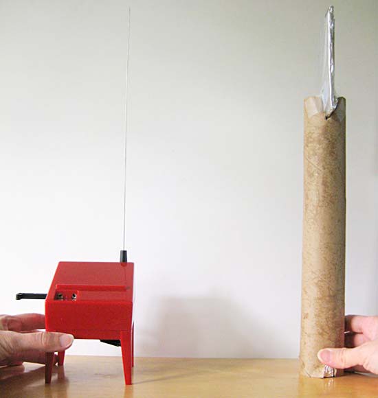 A theremin is placed across a cardboard tube that holds a square of aluminum foil at the top end