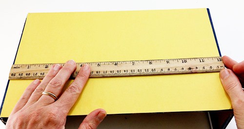 A line being drawn on a shoebox parallel to the long side of the box. 