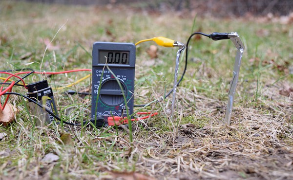 Leads of a multimeter attach to two aluminum foil props placed in the soil