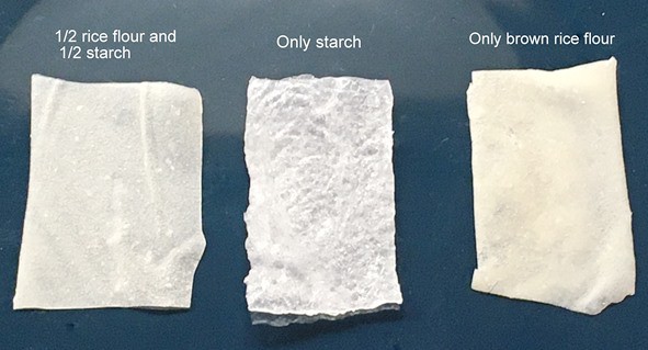 Three rectangles of edible paper on a dark background. The type of flours used for each paper are written above each piece.