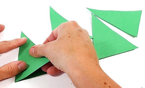 Three paper triangles on a table. Hands holding a gluestick and applying glue to an additional paper triangle. 