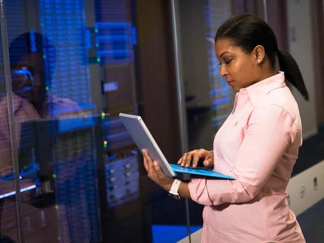 Woman in front of servers looking at laptop