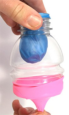 The top-half of a cut plastic bottle is covered on both ends by deflated balloons