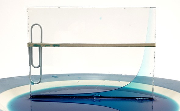 Blue liquid moves up the right side of two glass panes that are pressed together