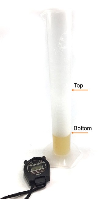  A measuring cylinder on a table. Two arrows indicate the top and bottom of the foam layer. Next to the measuring cylinder lies a stop watch. 