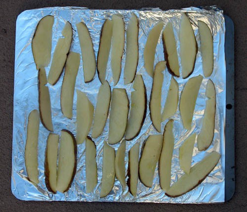 Raw potato wedges spaced evenly and laid flat on a tin-foil lined baking sheet