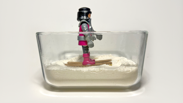 Toy action figure on cardboard skis in a container of flour