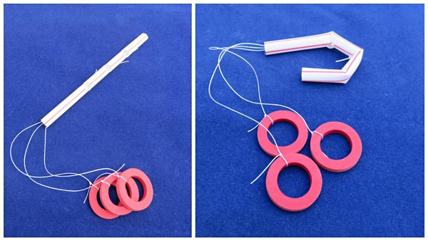 Three strings threaded through the inside of a straw are tied to small red rings