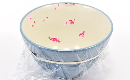 Bowl with colorful sprinkles vibrating on top of tightly-wrapped plastic. 