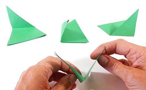 Three folded paper triangles on a table. Hands holding one paper triangle opening the fold so it looks like a V-shape. 