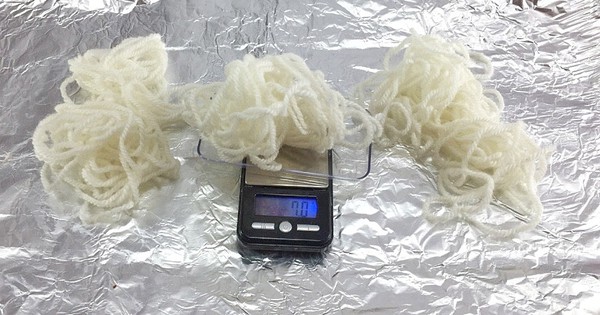 One piece of wool yarmn is lying on a digital scale. Two pieces of wool yarn are lying next to the scale. 