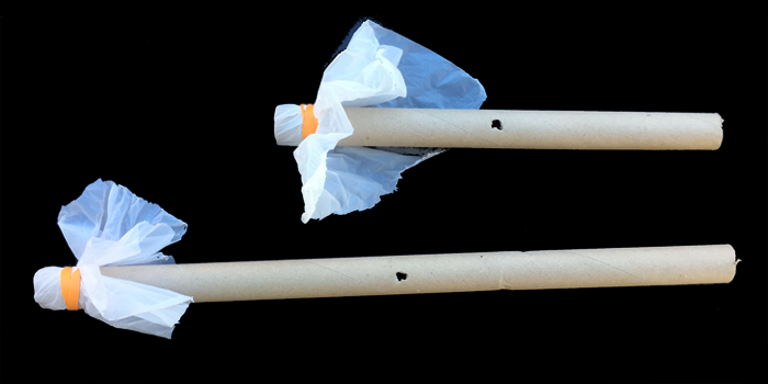 Two homemade kazoos made from a cardboard tube with plastic sheets held over one end with a rubber band