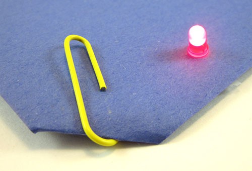 A paperclip holds a battery against the back of a sheet of paper