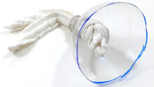 Two cotton strips tied together are pushed through the mouth of a cut plastic bottle