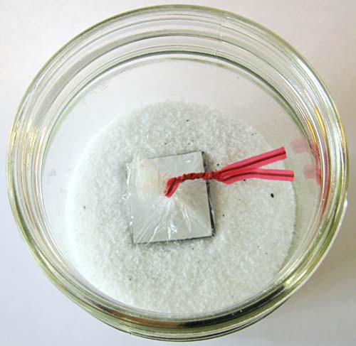 A magnetic square wrapped in plastic is dropped into a jar filled with iron filings and salt