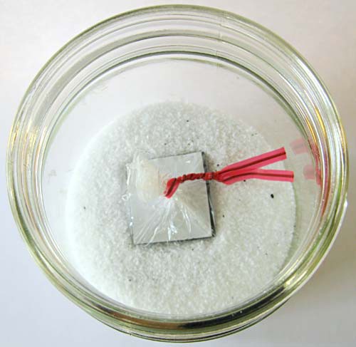 A magnetic square wrapped in plastic is dropped into a jar filled with iron filings and salt