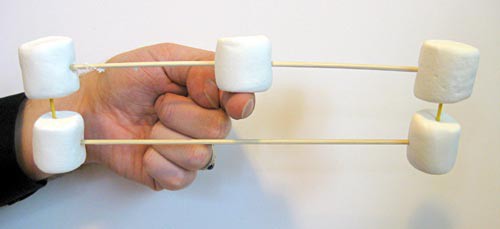 a hand attempting to balance a frame made of marshmallows and skewers