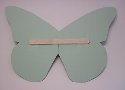 A popsicle stick is taped across the wings of a paper butterfly cutout