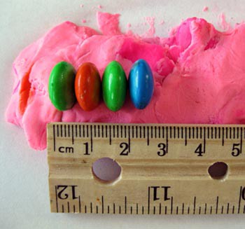 Four M&M candies are stacked horizontally on a piece of putty and measured in length