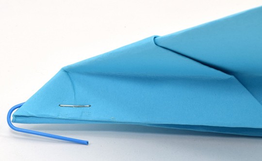 A paper clip attached to the nose of a paper airplane. 