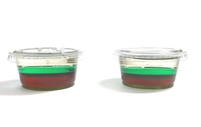 Two mini cups filled with corn syrup, green water, and vegetable oil and showing the layering of the different liquids. 