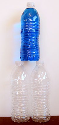 A full water bottle is stacked on the lids of two empty water bottles