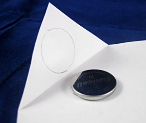 A coin cell battery is traced on the corner of a piece of paper