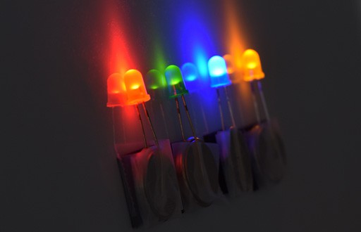 Four LEDs of different colors are taped to button cell batteries and attached to a magnets on a wall