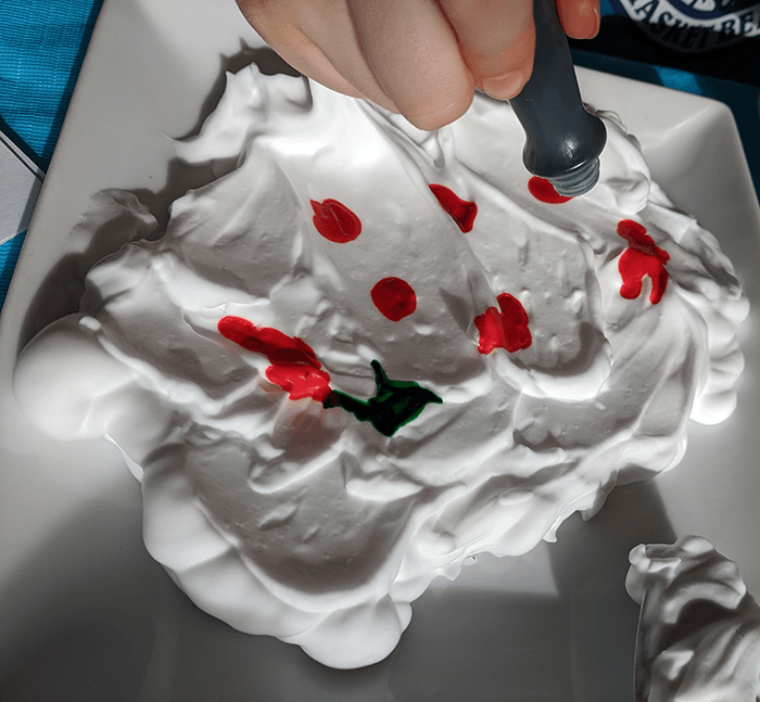 Student adding drops of food coloring on top of shaving cream