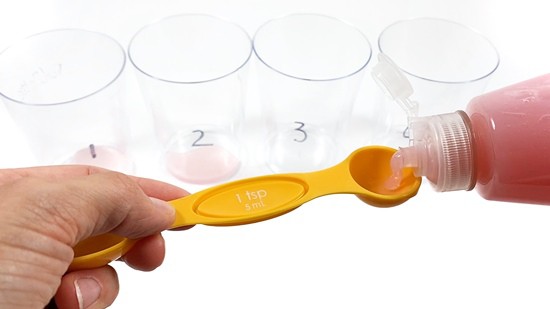A person squeezes dish soap into a measuring spoon.