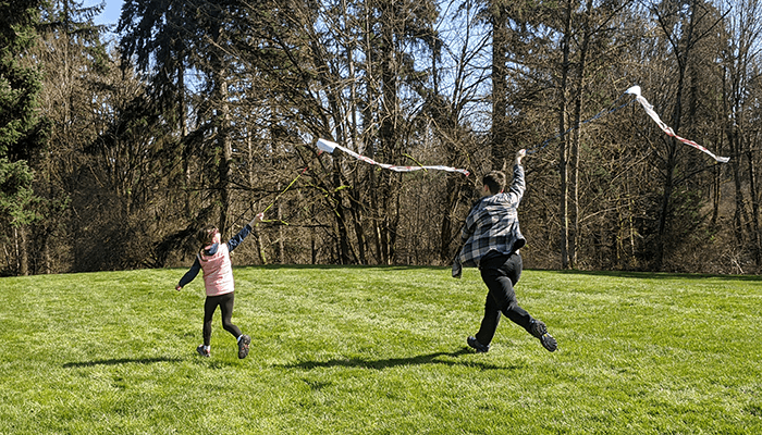 Two students running in a grassy open area flying homemade kites