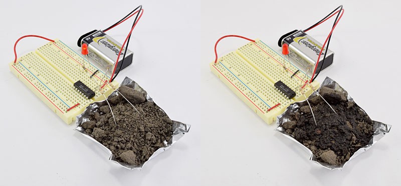Two leads from a moisture sensor are inserted into a pile of dry soil and a pile of wet soil