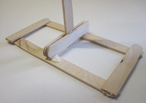 The base of a popsicle stick support is glued perpendicularly to a rectangular base made from popsicle sticks