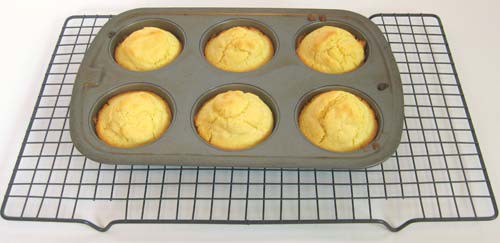 Six muffins in a muffin pan rest on a wire rack