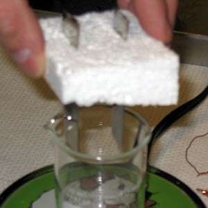 Two strips of metal stick through a block of styrofoam going into beaker