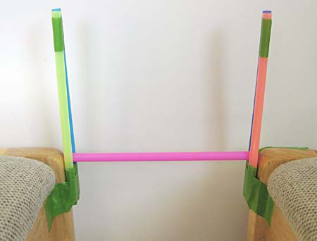 A straw rests length-wise between two tower bridges made of straw