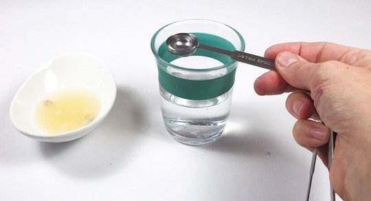 Half a teaspoon of water is added to a small bowl filled with lemon juice.